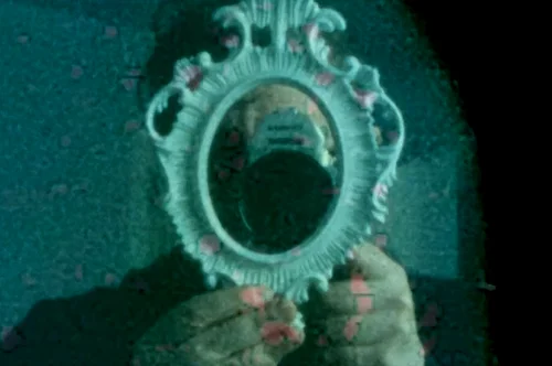 A grainy blue tinted image of a camera lens framed by a ornate white oval shaped frame.